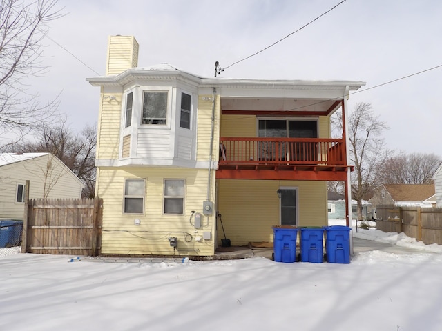 snow covered house with a balcony, a chimney, and fence