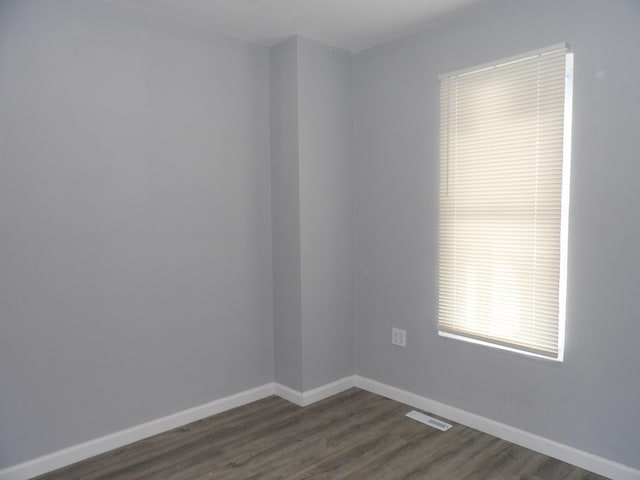 unfurnished room with baseboards, visible vents, and dark wood-type flooring