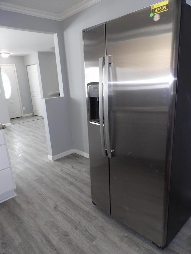 kitchen with wood finished floors, baseboards, white cabinets, stainless steel fridge, and crown molding