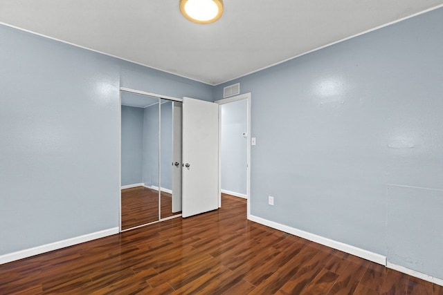 unfurnished bedroom with a closet, wood finished floors, visible vents, and baseboards