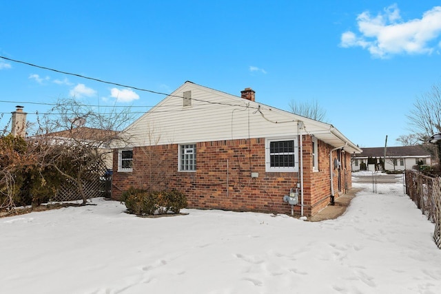 snow covered house featuring brick siding, fence, and a chimney