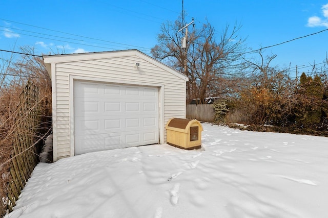 snow covered garage with a detached garage and fence