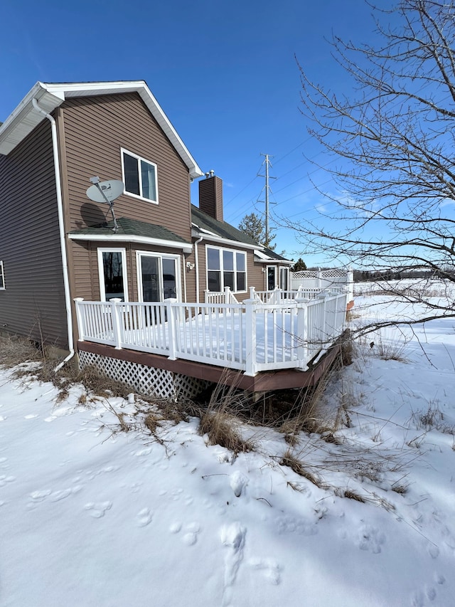 snow covered rear of property with a chimney and a deck