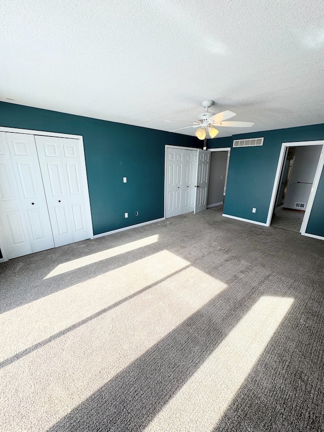 unfurnished bedroom featuring a textured ceiling, carpet floors, visible vents, baseboards, and multiple closets