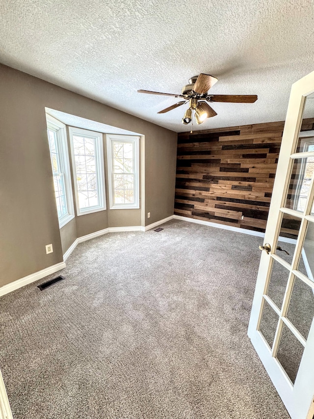 spare room with wood walls, carpet, visible vents, and a ceiling fan