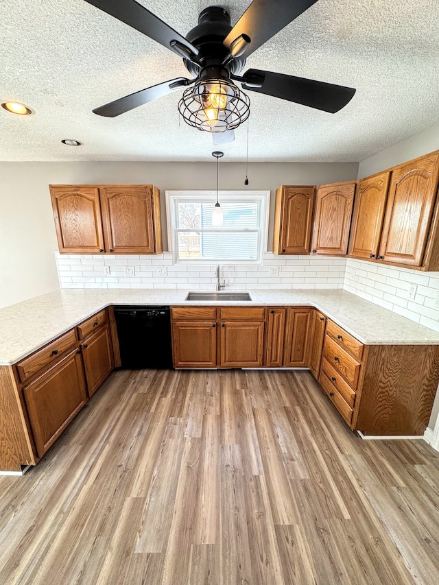 kitchen with brown cabinetry, dishwasher, a peninsula, light wood-style floors, and a sink