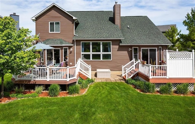 back of property featuring a shingled roof, a lawn, a chimney, and a wooden deck