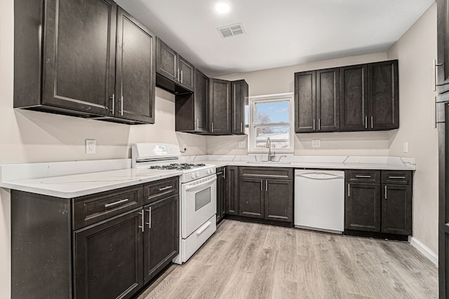 kitchen featuring visible vents, light wood-style floors, a sink, dark brown cabinets, and white appliances