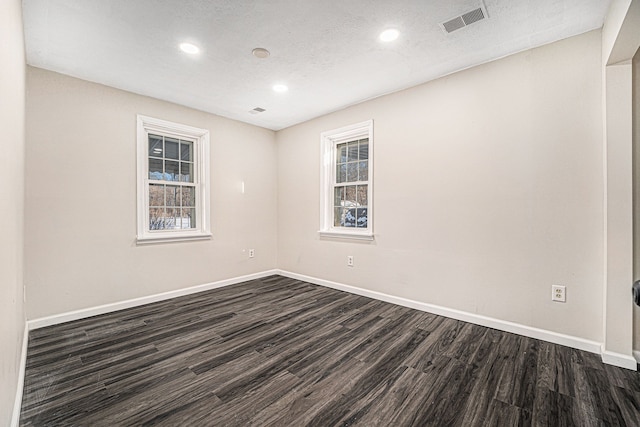 unfurnished room featuring a wealth of natural light, dark wood-type flooring, visible vents, and baseboards