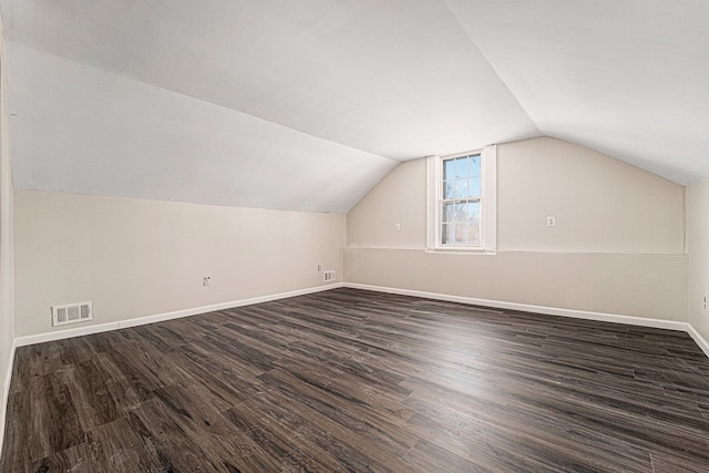 additional living space featuring dark wood-style floors, visible vents, vaulted ceiling, and baseboards