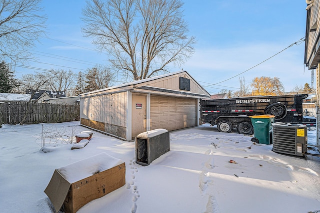 snow covered garage with a detached garage, fence, and central AC unit