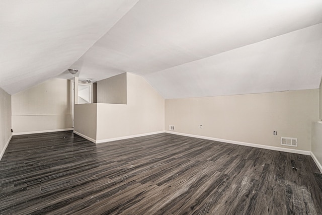 additional living space featuring visible vents, baseboards, vaulted ceiling, and dark wood-style flooring