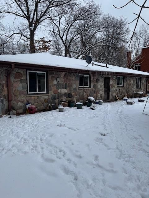 snow covered back of property with stone siding