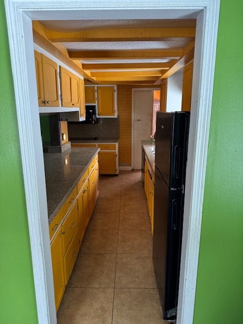 kitchen with light tile patterned flooring, beamed ceiling, and freestanding refrigerator