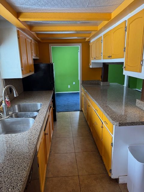 kitchen featuring black dishwasher, beamed ceiling, tile patterned flooring, a textured ceiling, and a sink