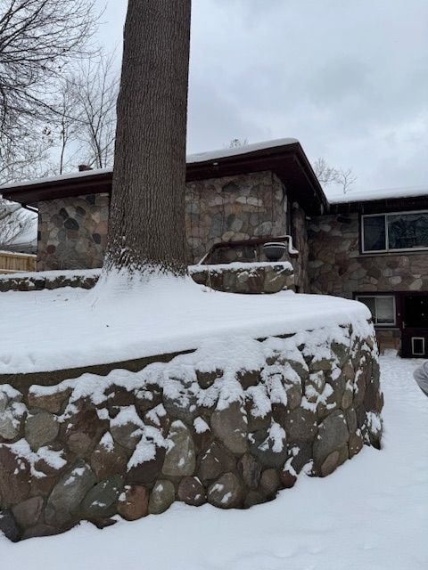 view of snow covered exterior with a garage and stone siding