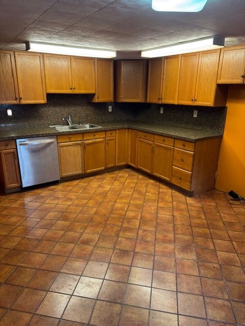 kitchen featuring stainless steel dishwasher, dark countertops, a sink, and tasteful backsplash