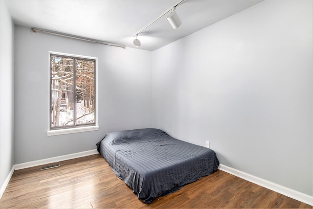 bedroom with baseboards, track lighting, visible vents, and wood finished floors