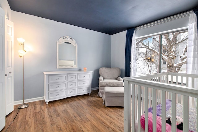 bedroom featuring a nursery area, baseboards, and wood finished floors