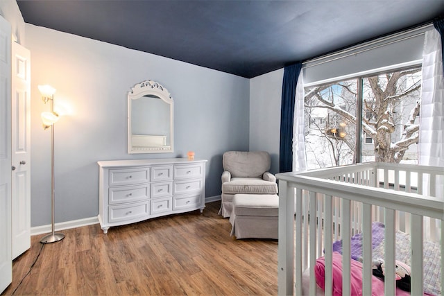 bedroom with a nursery area, baseboards, and wood finished floors