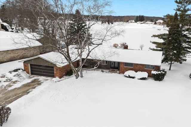 snow covered property with a garage and brick siding