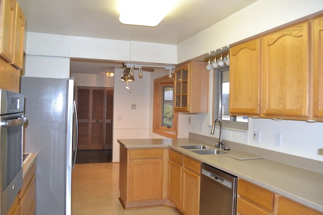 kitchen featuring light wood-type flooring, light countertops, appliances with stainless steel finishes, a peninsula, and a sink