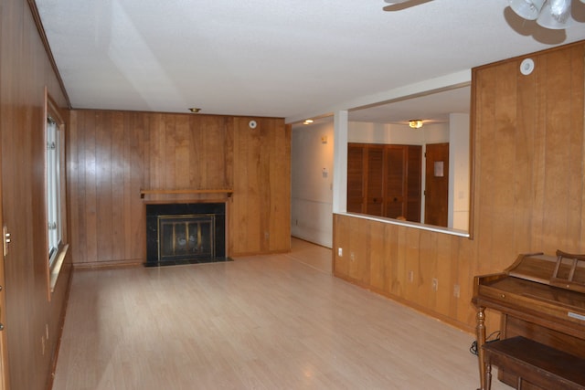 living room featuring a fireplace with flush hearth, wood finished floors, wood walls, and ceiling fan