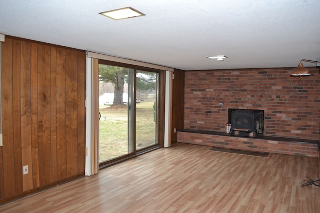 unfurnished living room with light wood finished floors, wooden walls, a wall of windows, and a wood stove