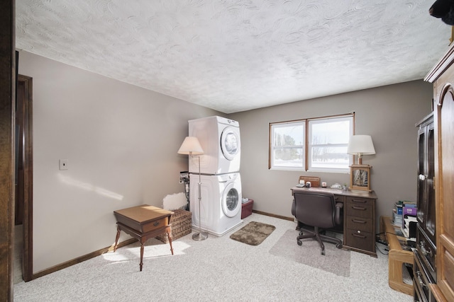 office space featuring baseboards, a textured ceiling, stacked washing maching and dryer, and light colored carpet