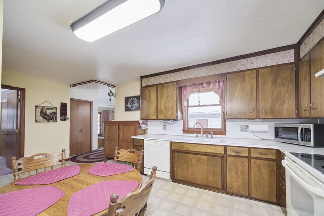 kitchen featuring light floors, light countertops, brown cabinetry, a sink, and white appliances