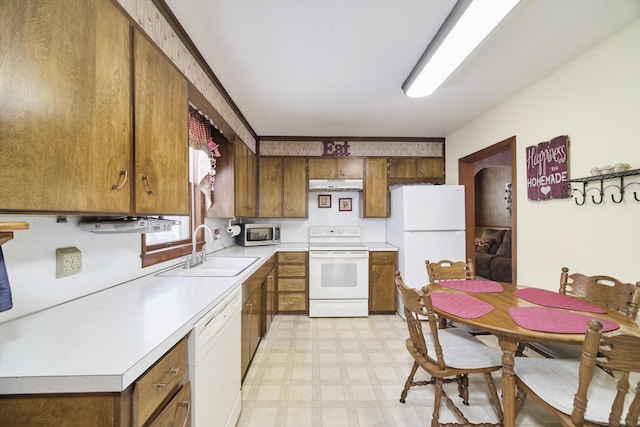 kitchen with under cabinet range hood, white appliances, a sink, light countertops, and light floors