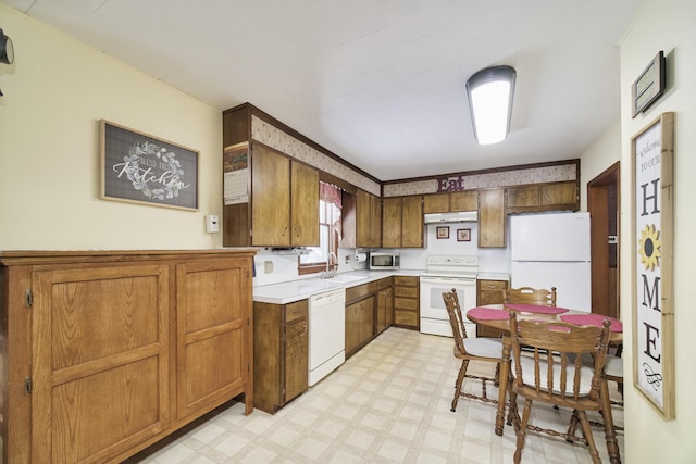 kitchen featuring under cabinet range hood, white appliances, a sink, light countertops, and light floors