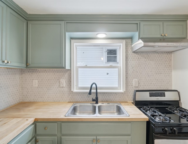 kitchen with gas range, green cabinets, under cabinet range hood, wooden counters, and a sink