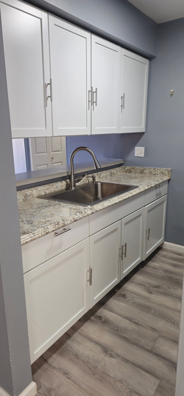 kitchen with dark wood finished floors, white cabinets, a sink, and light stone countertops