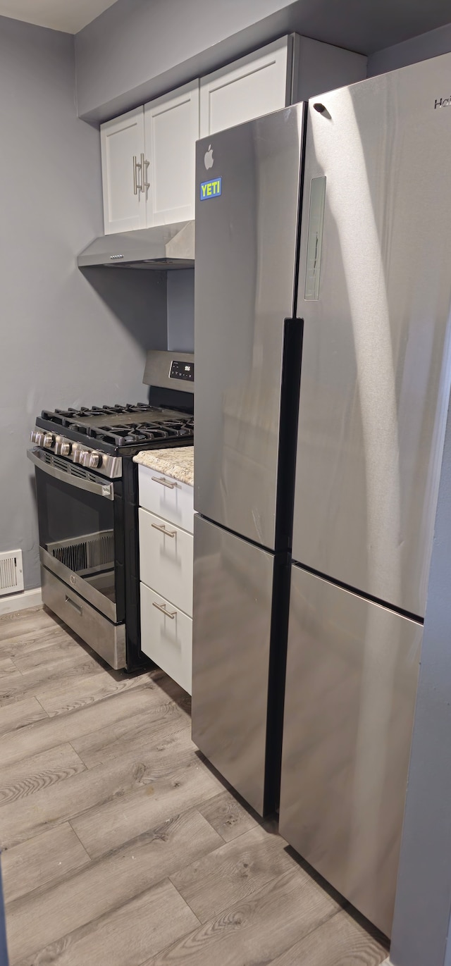 kitchen with visible vents, stainless steel appliances, wall chimney exhaust hood, and white cabinetry