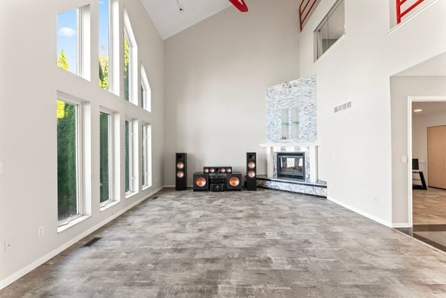 living room featuring visible vents, a towering ceiling, a glass covered fireplace, wood finished floors, and baseboards