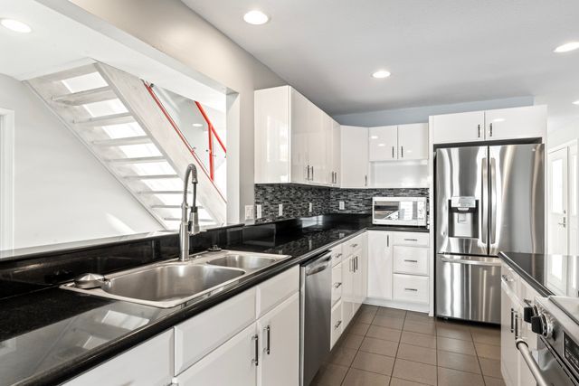 kitchen featuring dark tile patterned floors, a sink, white cabinetry, appliances with stainless steel finishes, and dark countertops