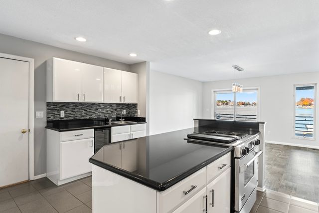 kitchen featuring stainless steel range, white cabinets, dark countertops, hanging light fixtures, and a healthy amount of sunlight