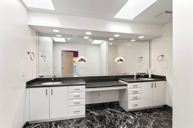 bathroom with marble finish floor, two vanities, and a sink