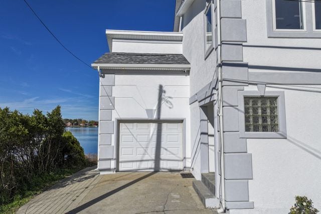 exterior space with a garage, a water view, concrete driveway, and stucco siding