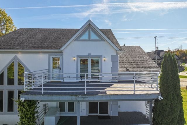 back of house featuring a shingled roof, a balcony, and stucco siding