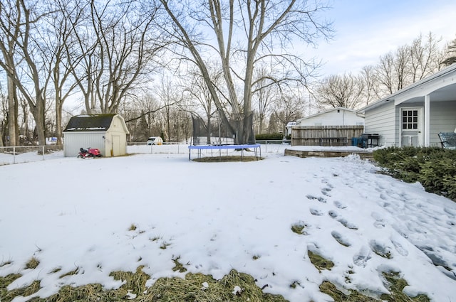 yard covered in snow featuring a trampoline, an outdoor structure, a storage shed, and fence