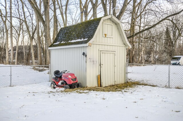 snow covered structure featuring fence, a storage unit, and an outbuilding