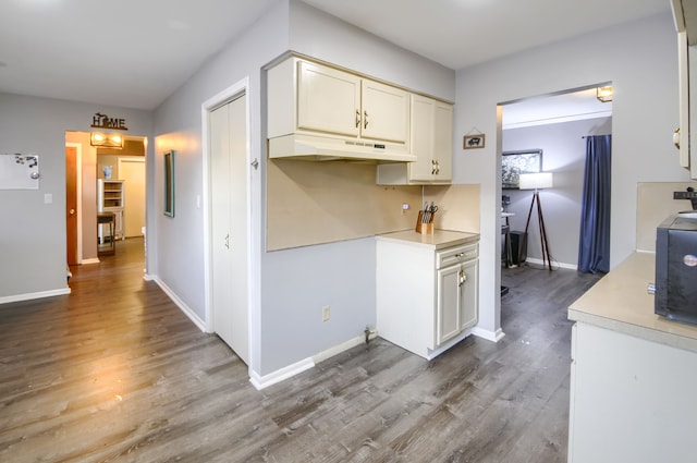 kitchen featuring baseboards, light countertops, wood finished floors, and under cabinet range hood