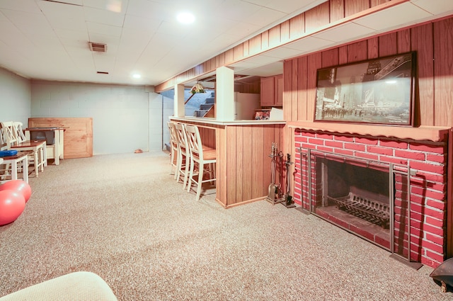 bar featuring concrete block wall, a bar, wood walls, carpet floors, and a brick fireplace