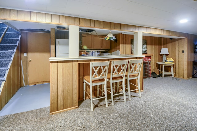 kitchen featuring wooden walls, light colored carpet, a breakfast bar, brown cabinets, and white fridge