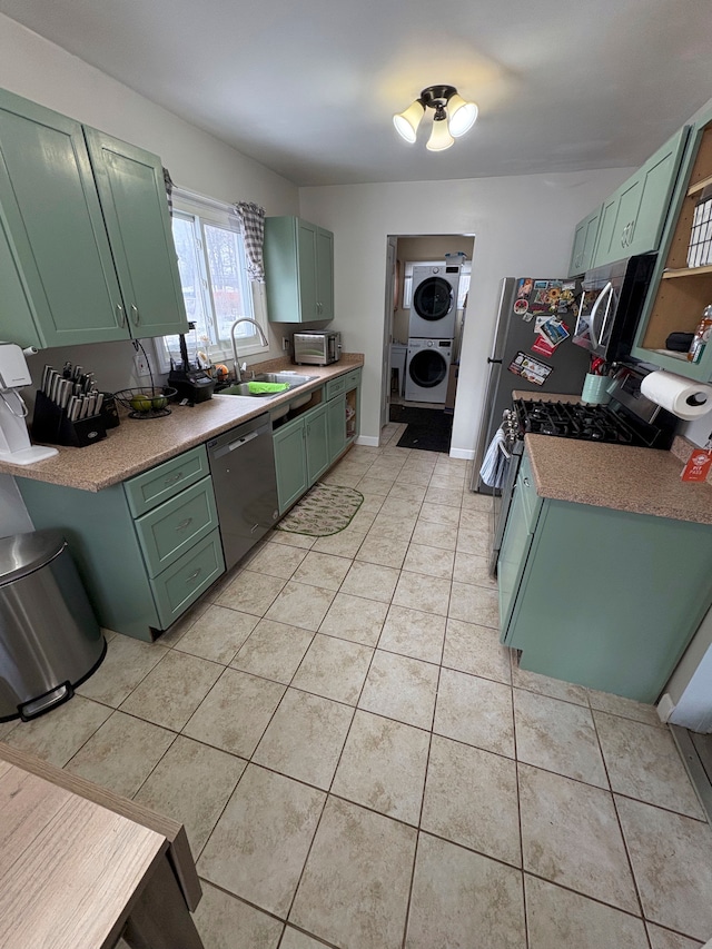 kitchen with light tile patterned floors, stacked washer / drying machine, green cabinets, appliances with stainless steel finishes, and a sink