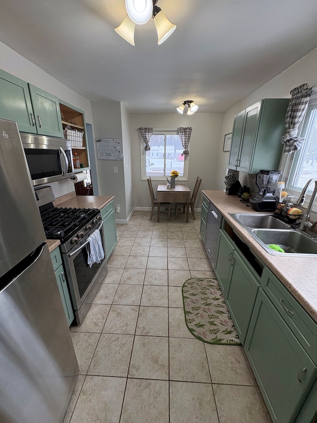 kitchen with light tile patterned floors, ceiling fan, stainless steel appliances, a sink, and green cabinets