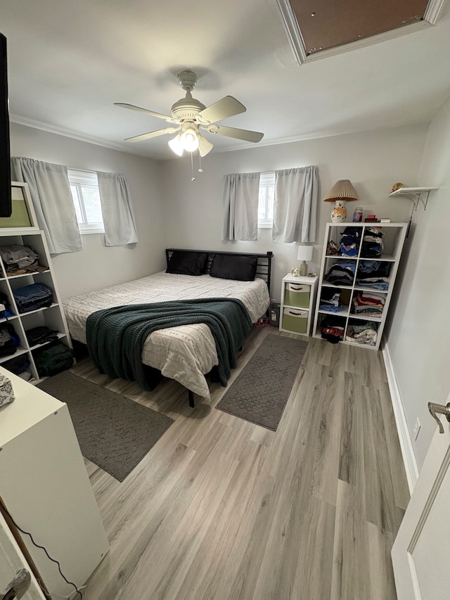 bedroom featuring ceiling fan, wood finished floors, baseboards, ornamental molding, and attic access