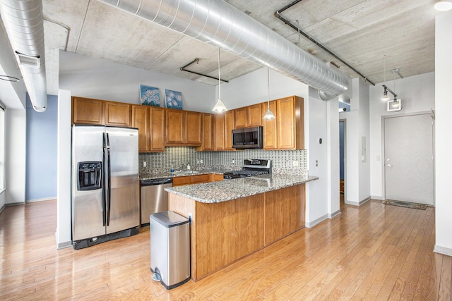 kitchen featuring light stone counters, brown cabinets, decorative light fixtures, stainless steel appliances, and a peninsula